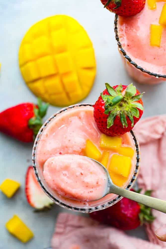 The top view of a glass with strawberry mango smoothie in it and a spoon scooping some out. 