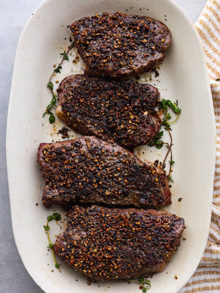 Top-down view of 4 steaks on a white serving dish.