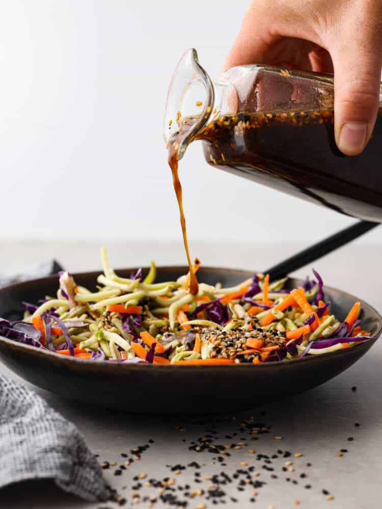 Dressing being poured over a bowl of vegetables.