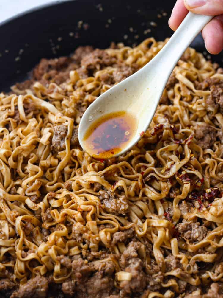 Close up view of chili oil being spooned over a noodle dish.