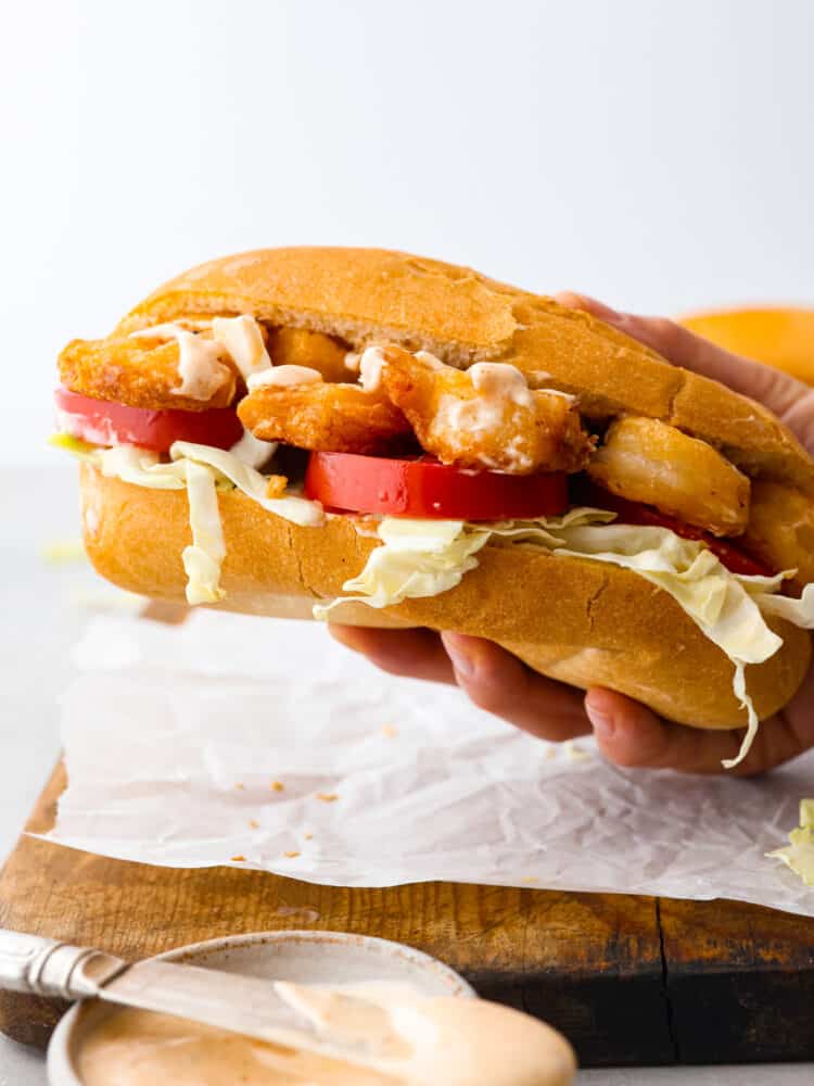 Close up side view of a hand holding a shrimp po boy sandwich.