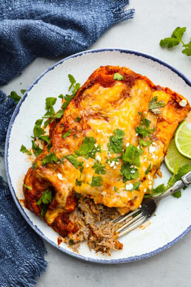 Top-down view of pork enchiladas, garnished with cilantro, on a blue and white plate.