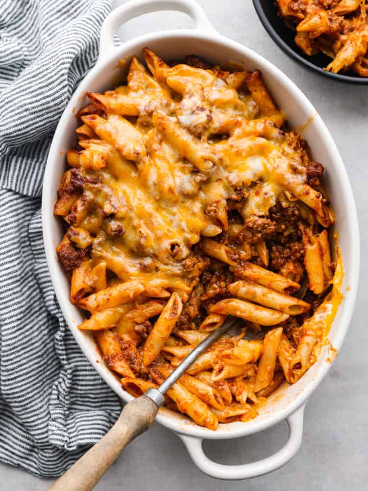 Top view of sloppy Joe casserole in a white baking dish. A striped blue and white towel and black bowl filled with casserole are next to the baking dish.