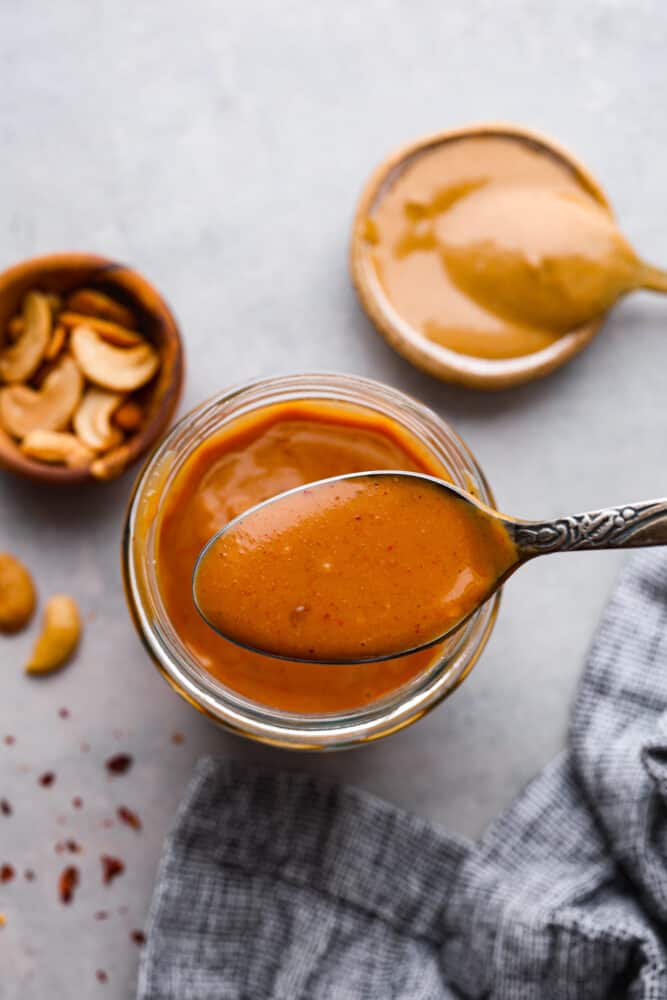 The top view of cashew dressing with a spoonful of the dressing being held over the top of the jar. 