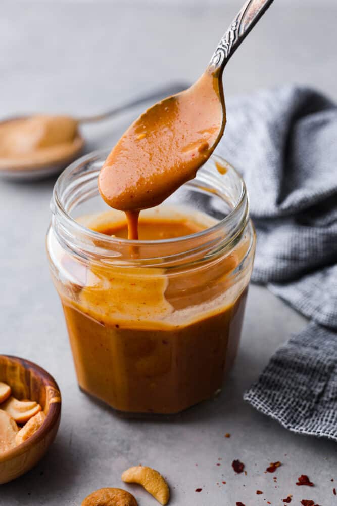 A jar of cashew dressing with a spoon scooping some out. 