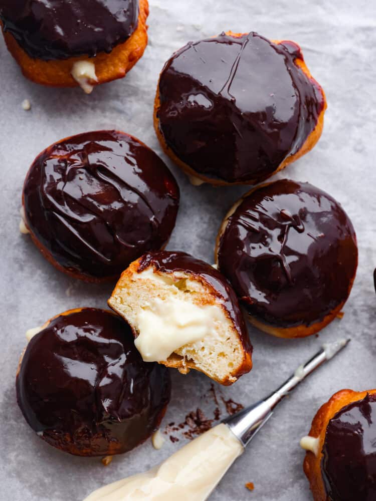 The top view of Boston cream donuts on parchment paper. One is cut open so you can see the cream inside. 