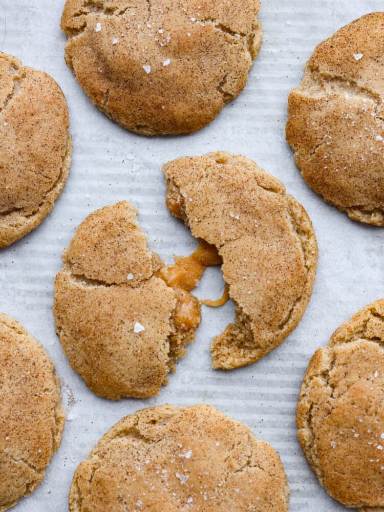 Top-down view of brown butter salted caramel snickerdoodles. One is broken in half, revealing a gooey caramel center.