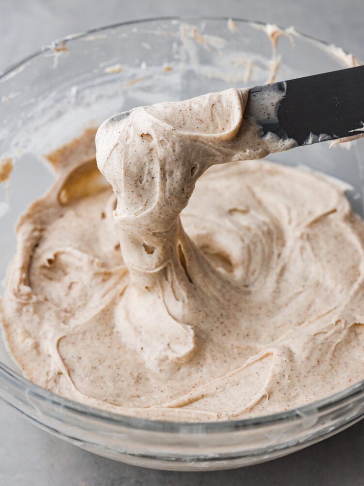 A knife being dipped into a bowl with cinnamon cream cheese frosting. 