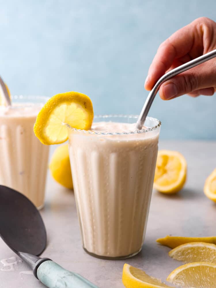 The side view of a frosted lemonade with a hand putting a straw in the glass. 