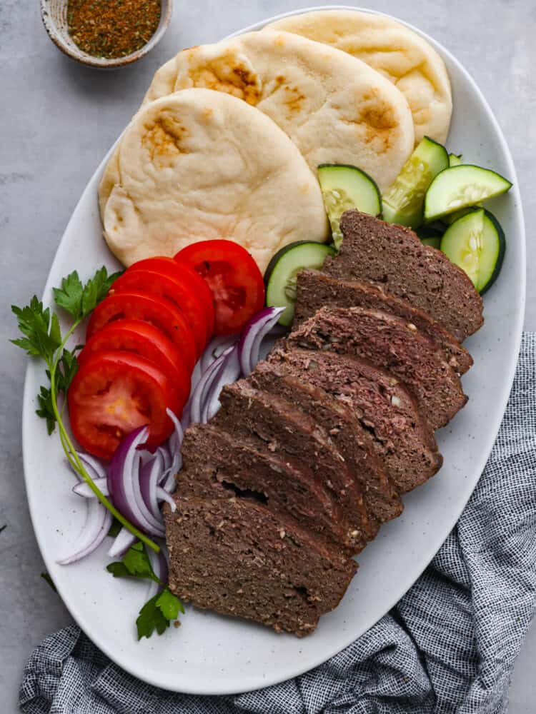 Sliced gyro meat served with tomatoes, onions, cucumber, and pita bread.