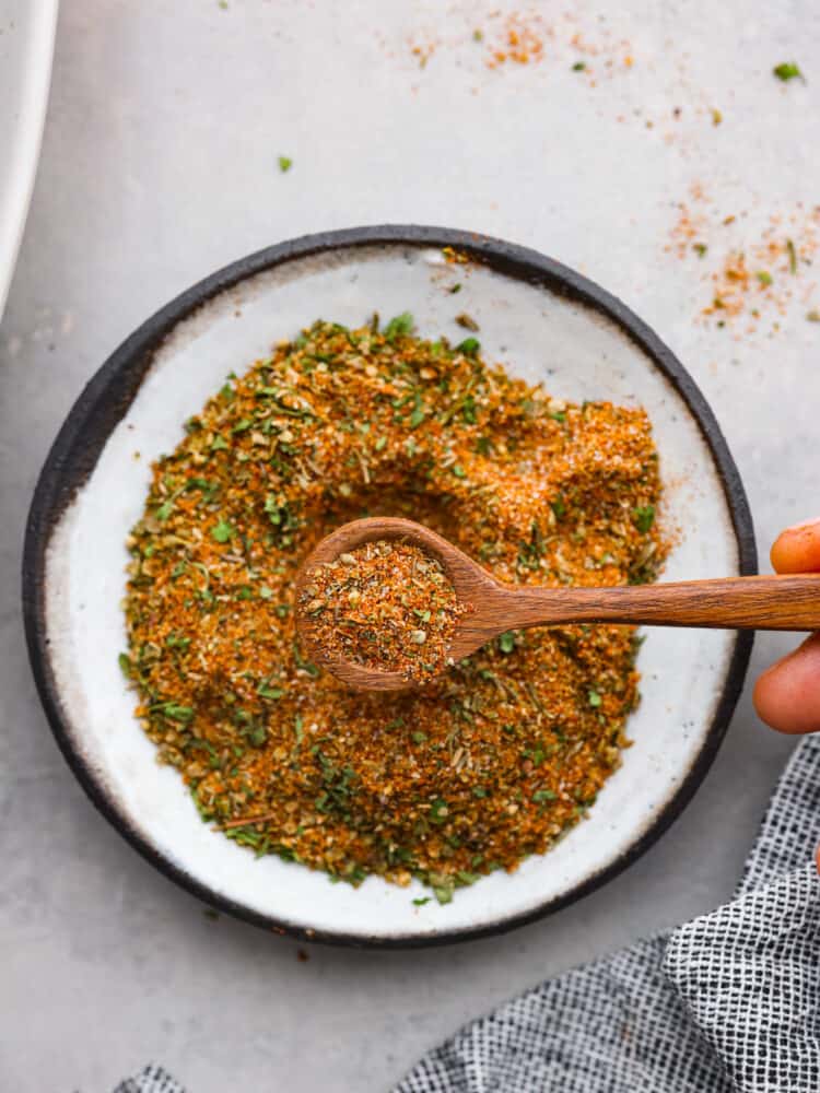 Close up view of gyro seasoning in a white bowl with a wood spoon. The spoon is lifting seasoning out of the bowl.