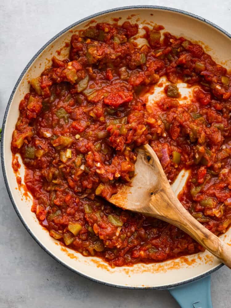 Close overhead view of salsa being stirred in a white skillet with a wooden spoon.