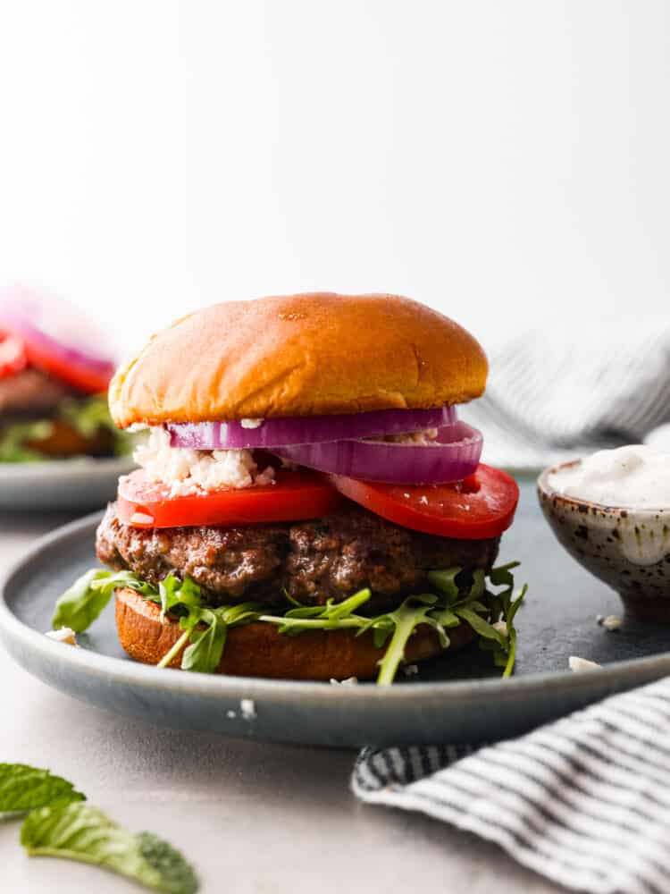 A lamb burger topped with tomatoes, onion, arugula, and feta cheese.