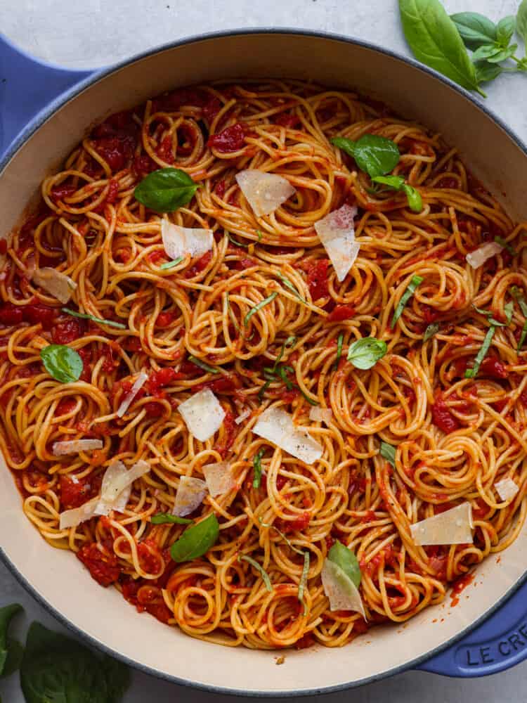 The top view of a pot of pasta pomodoro garnished with fresh cheese and mozzarella. 