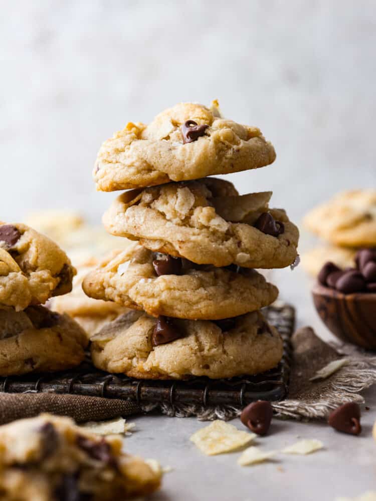 Close side view of stacked potato chip cookies on a cooking rack. A bowl of chocolate chips are next to the cookies.