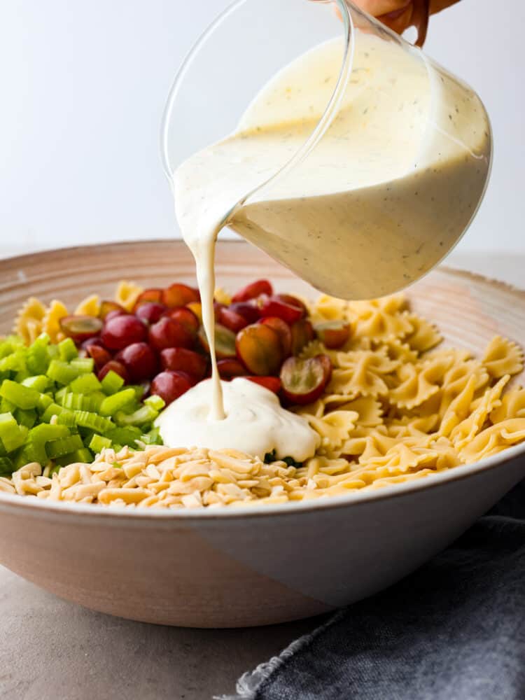 Dressing being poured over pasta salad ingredients. 