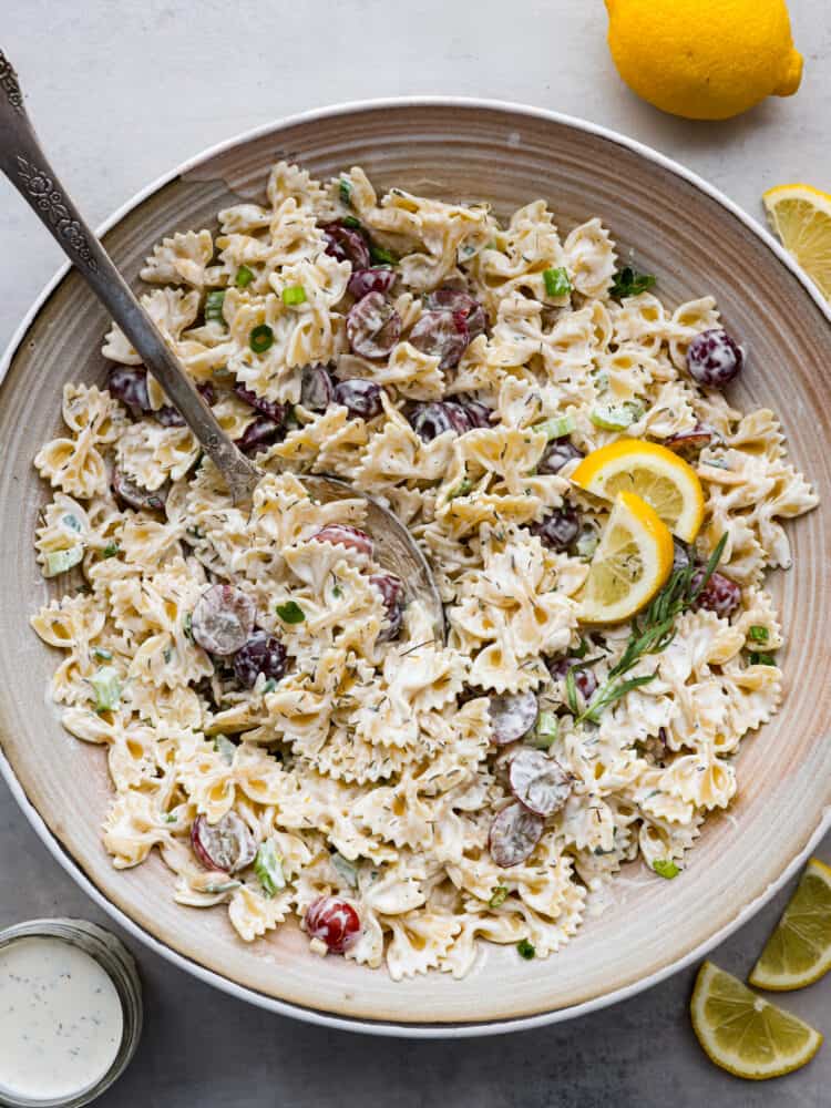 The top view of a large bowl with a silver spoon that has lemon tarragon pasta salad in it. 