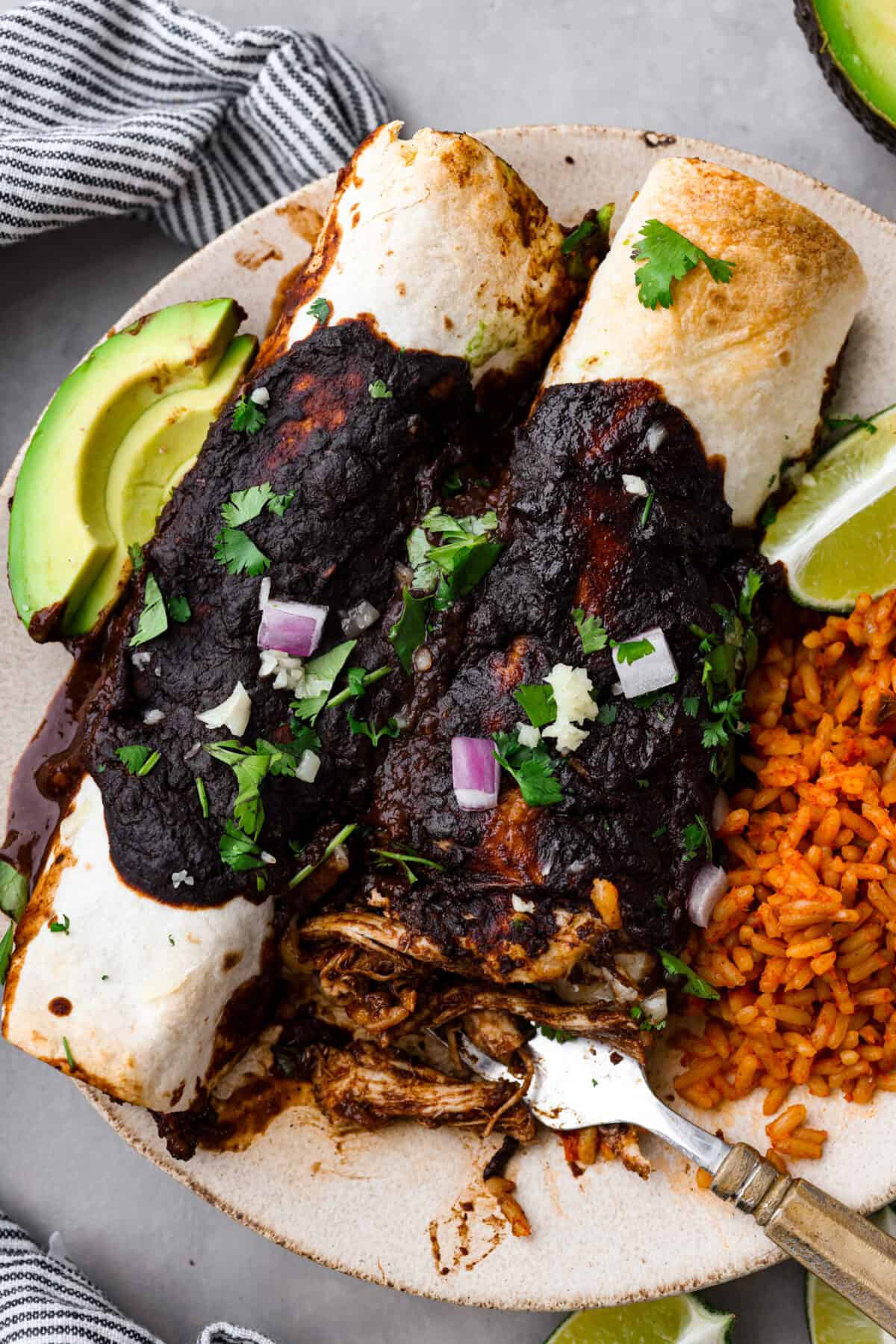 2 mole enchiladas served with rice on a stoneware plate.