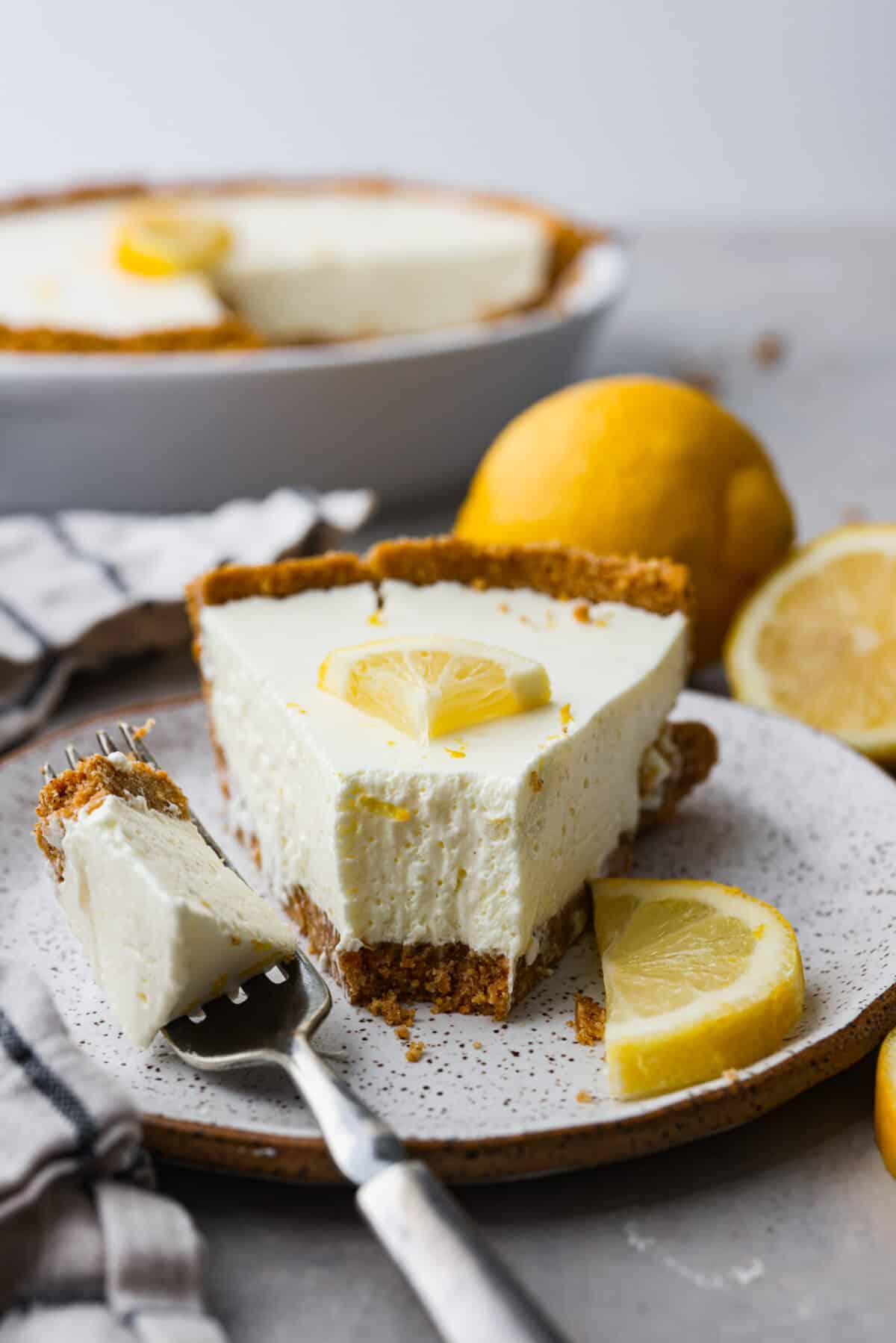 Close view of no-bake lemon pie on a white plate. Garnished with lemon slices and a fork on the plate.