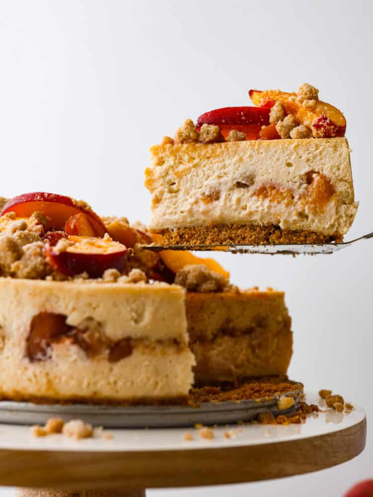 The side view of a slice of peach cobbler cheesecake being taken out with a pie server. 