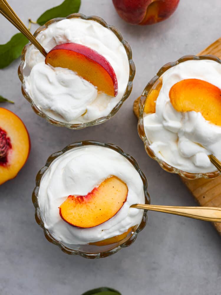 Top view of three glass dishes filled with peaches and cream. Gold spoons are nestled inside the dishes.