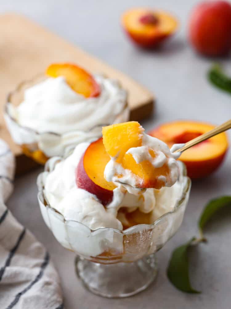 Close view of peaches and cream with a gold spoon lifting up peaches from the dish.