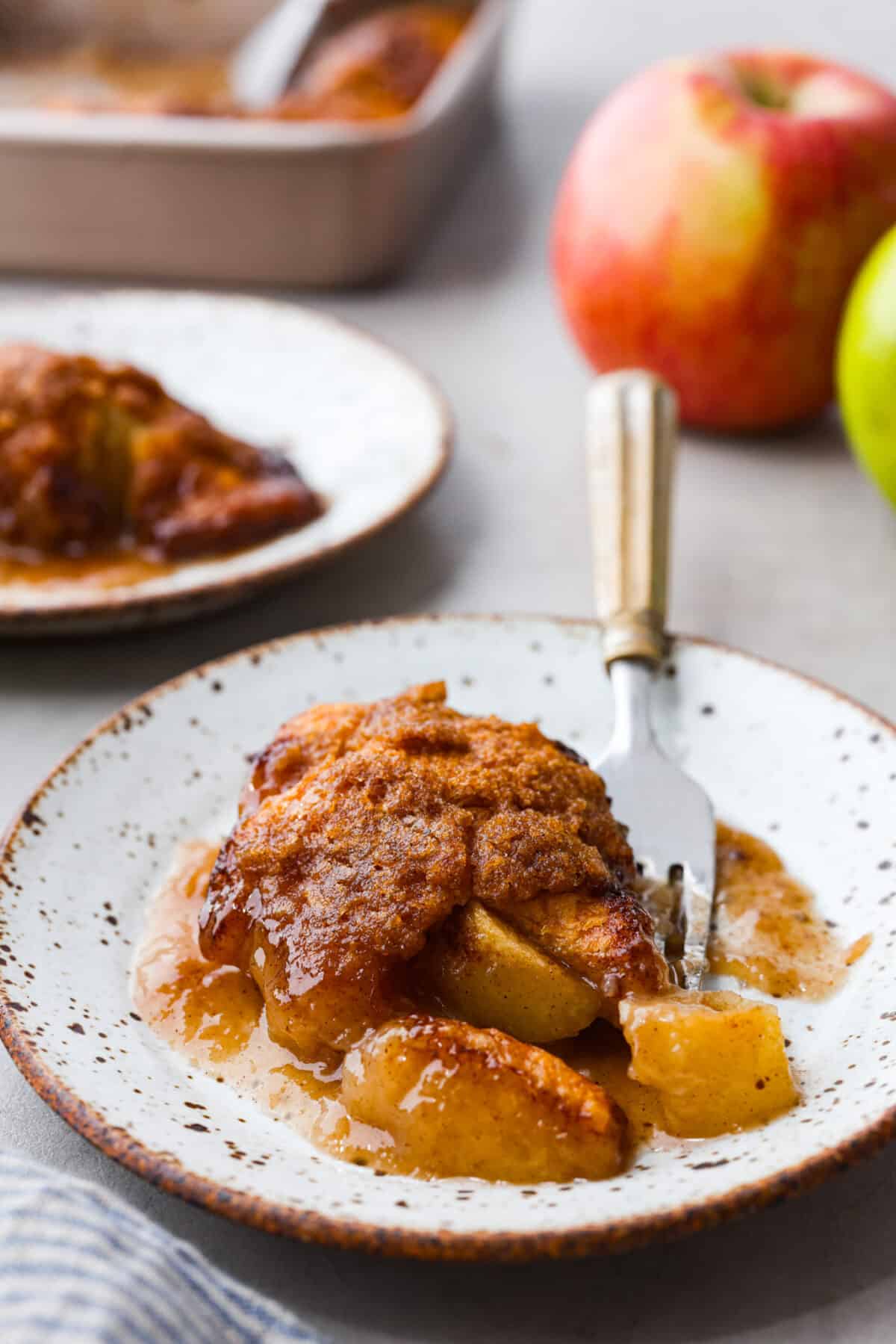 Baked apple dumplings on a white speckled plate with a fork.