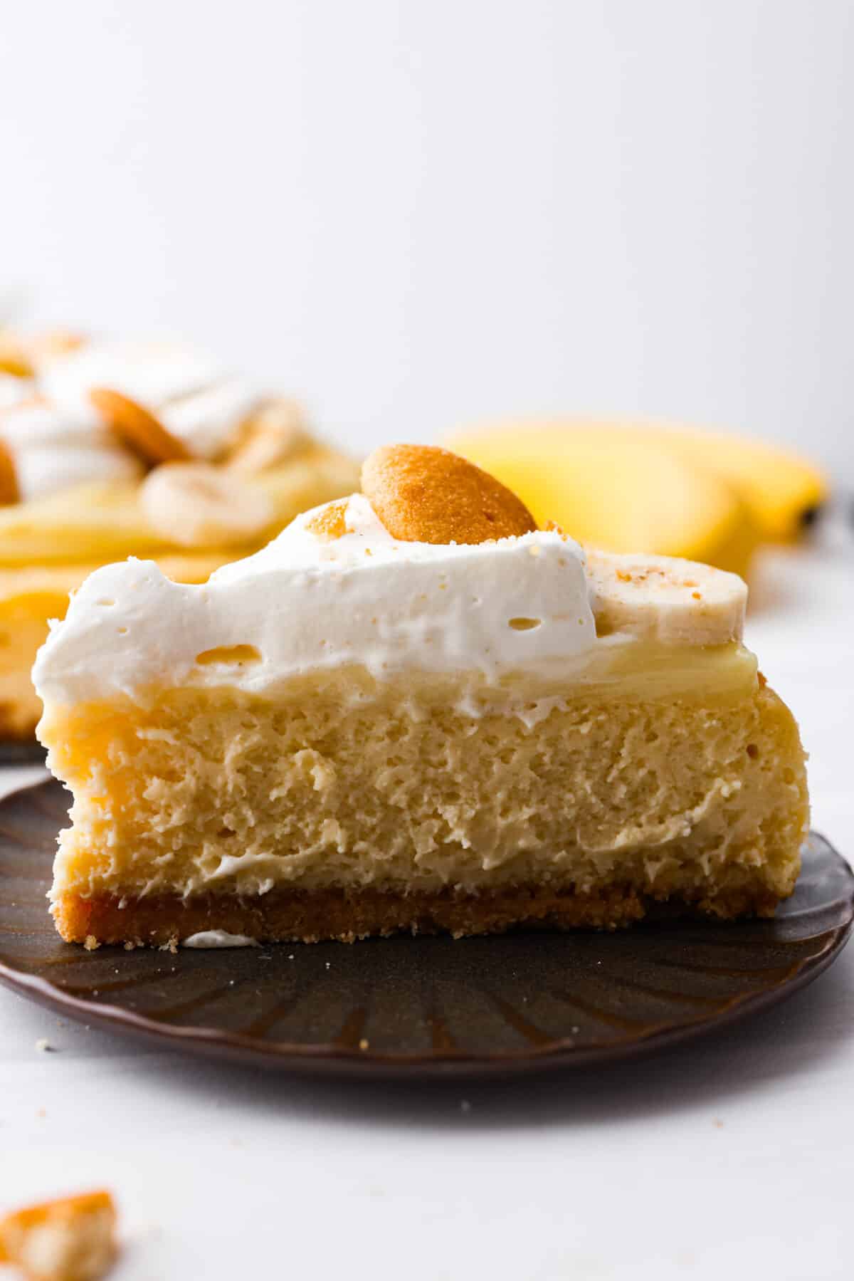 A slice of banana pudding cheesecake on a brown plate. 