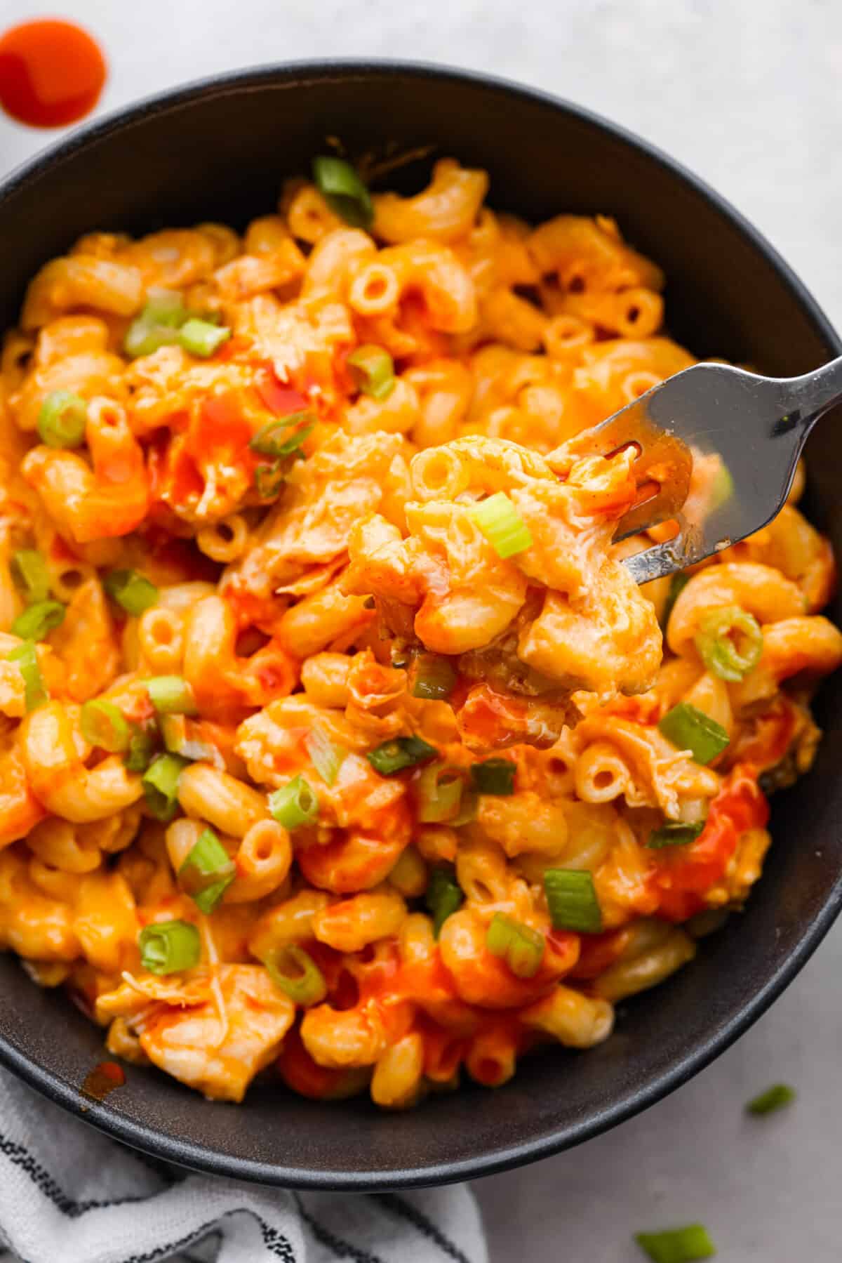 Close view of buffalo chicken mac and cheese in a black bowl with a silver fork lifting up macaroni.