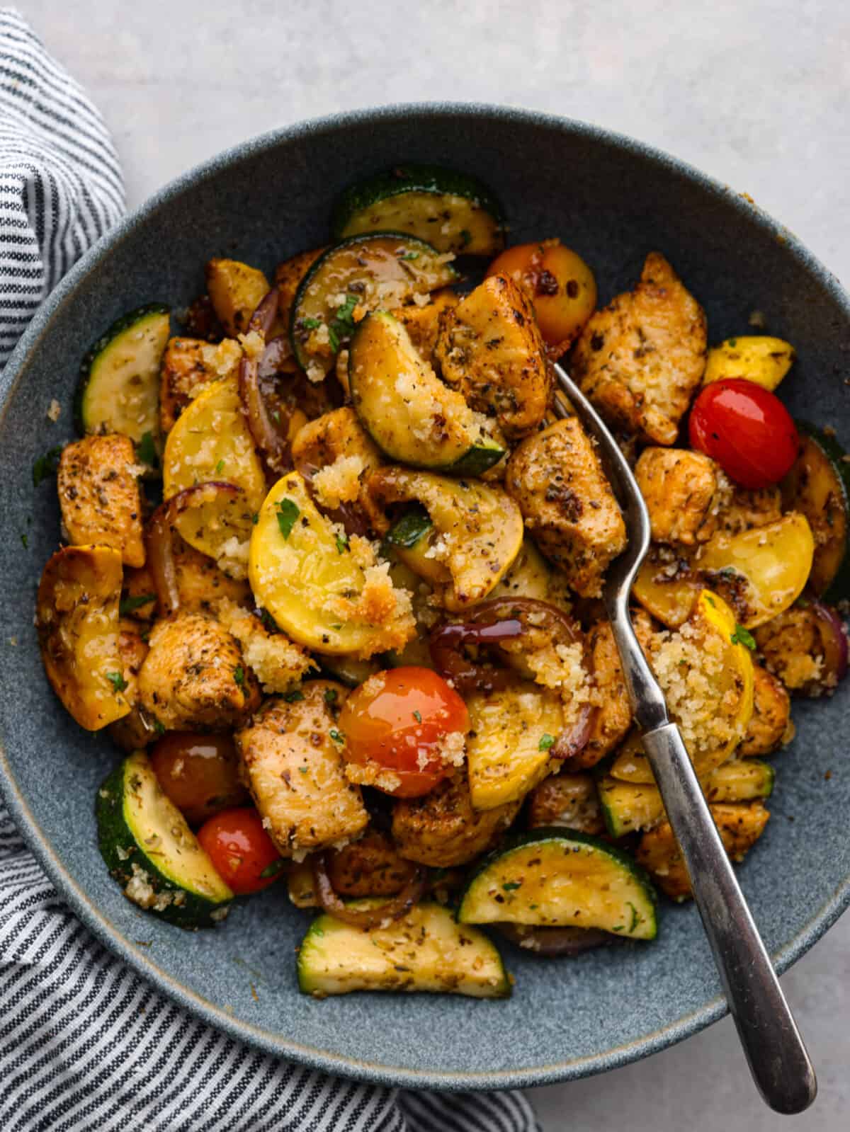 Close view of chicken and garden vegetables in a gray bowl with a fork in the bowl.