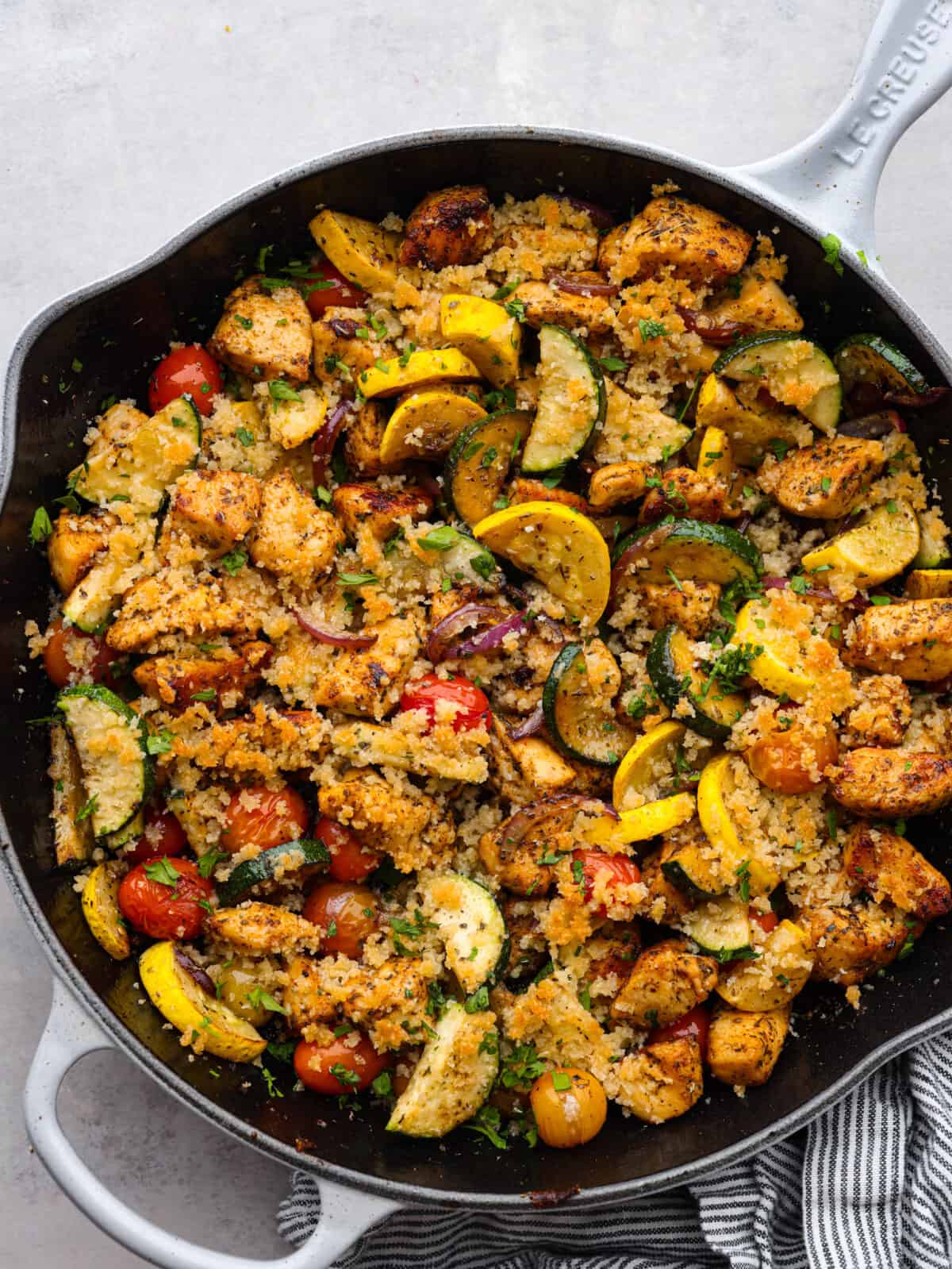 Top view of chicken and garden vegetables in a black skillet.