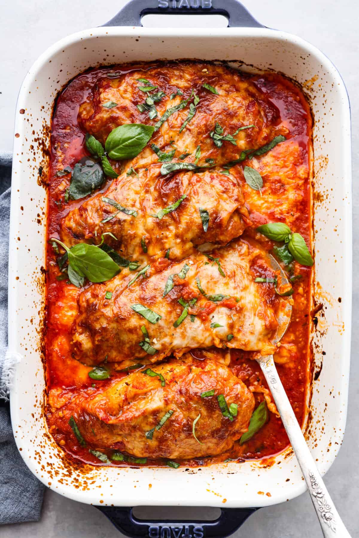 Top-down view of 4 chicken breasts coated in marinara sauce and cheese.