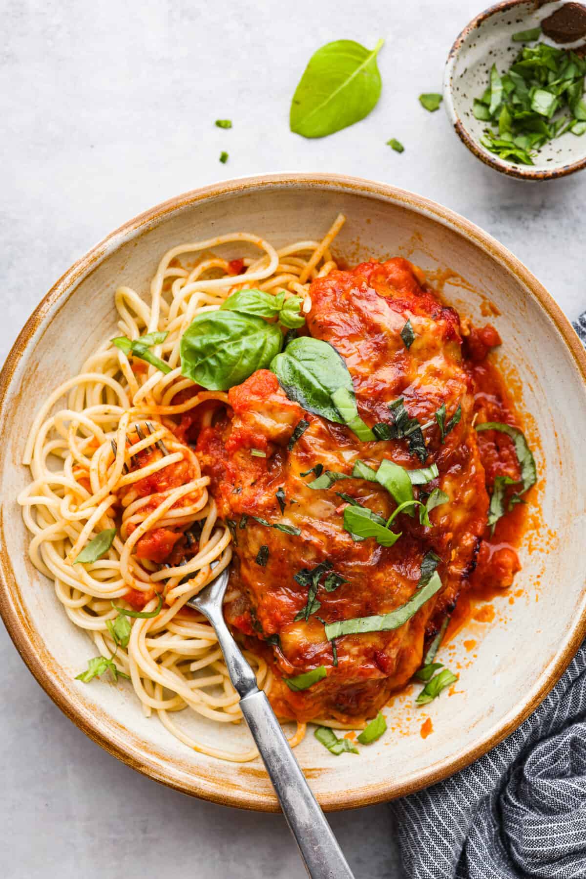 Chicken served with spaghetti noodles and fresh basil.