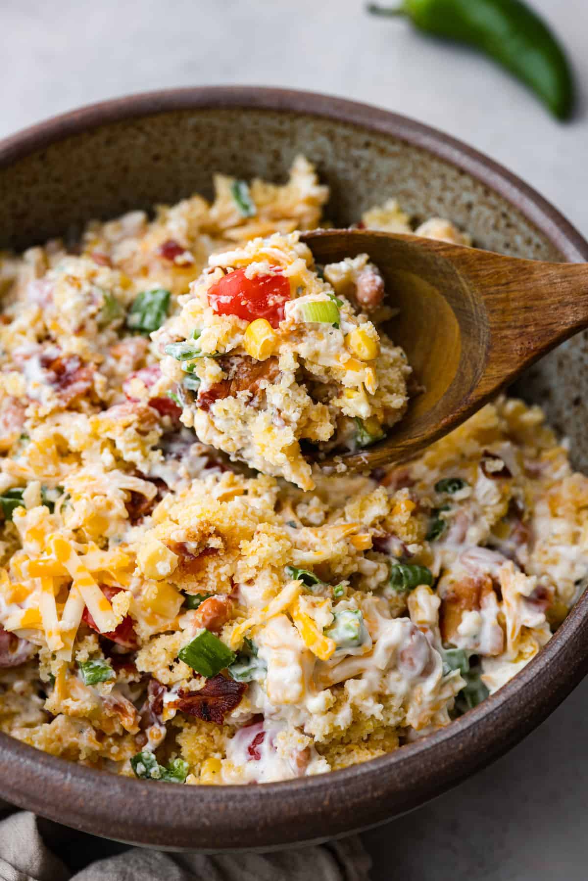 Close view of cornbread salad in a bowl with a wood spoon lifting up a spoonful of salad.