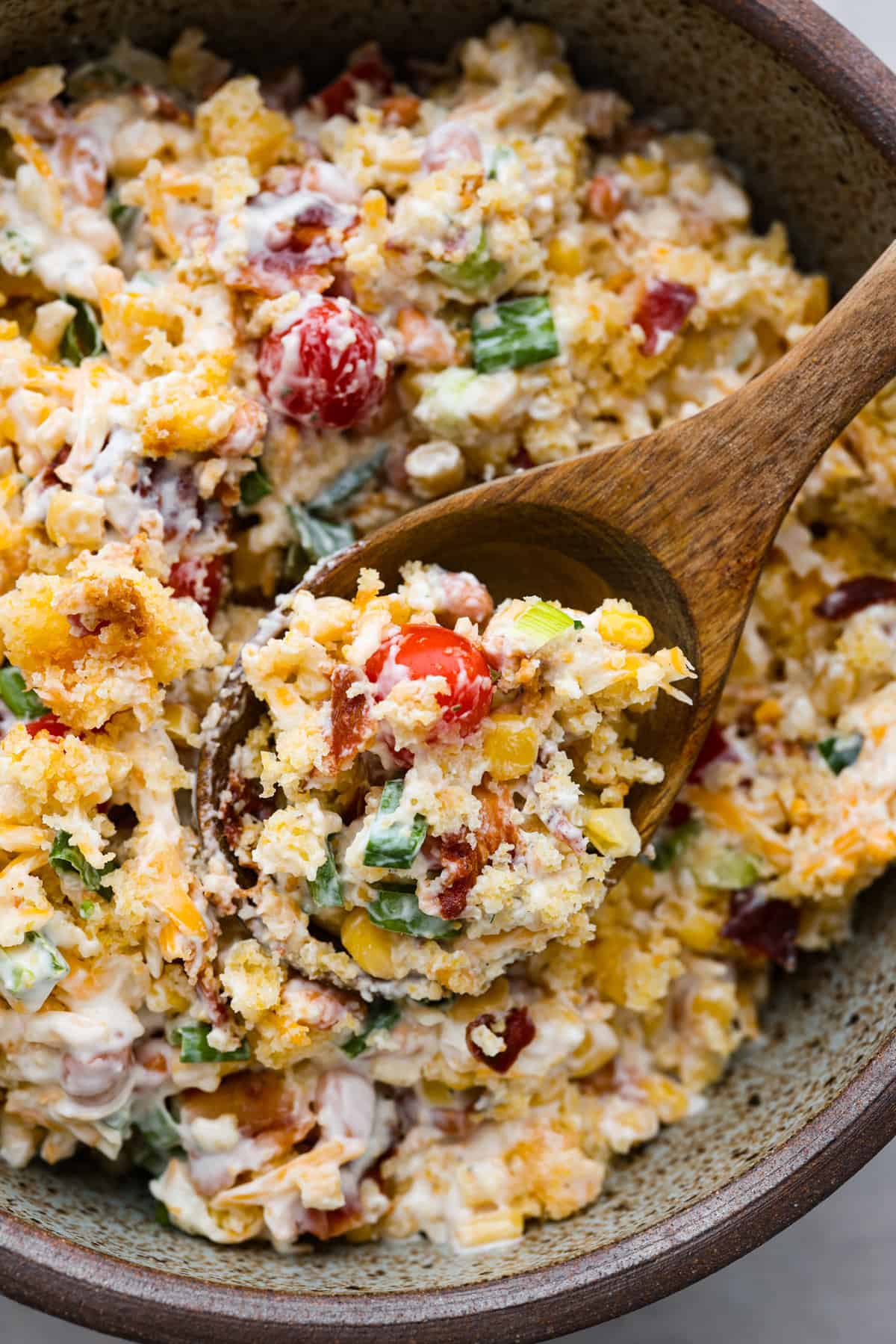 Close view of cornbread salad in a bowl with a wood spoon lifting up a spoonful of salad.