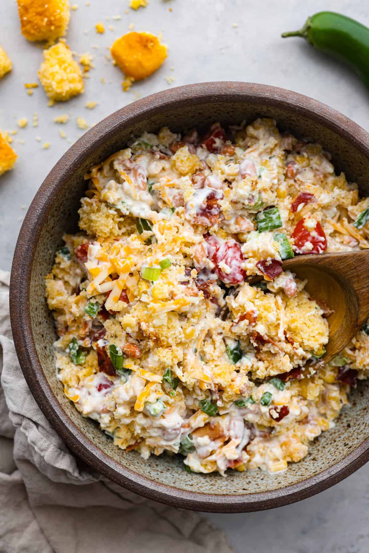 Top view of cornbread salad in a large brown bowl with a wooden spoon inside the bowl.