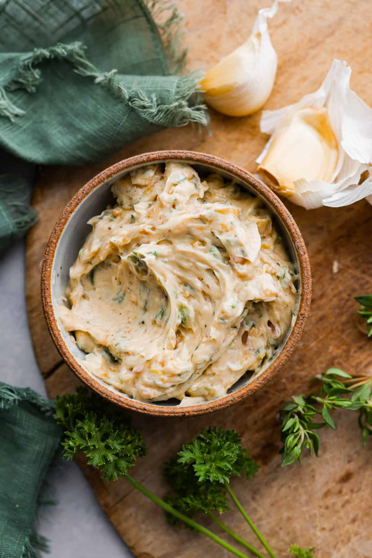 Top view of cowboy butter in a rustic bowl on a wood board with herbs and garlic next to the bowl.