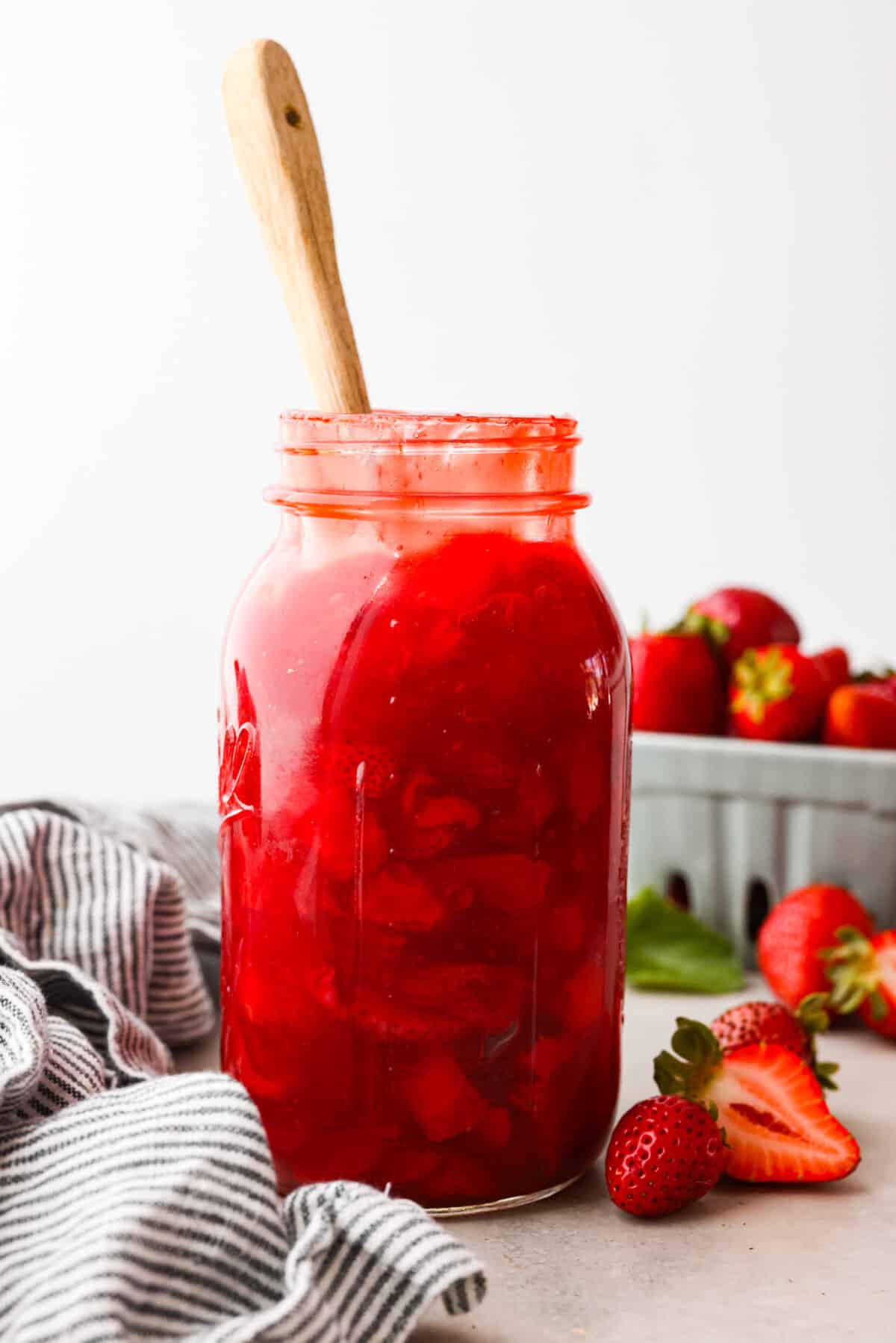 A jar of strawberry pie filling with a wooden spoon in it. 