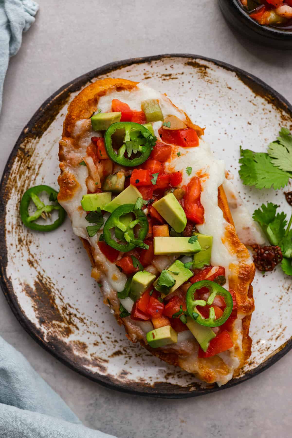 Closeup of molletes topped with pico de gallo, avocado slices, and jalapeno.