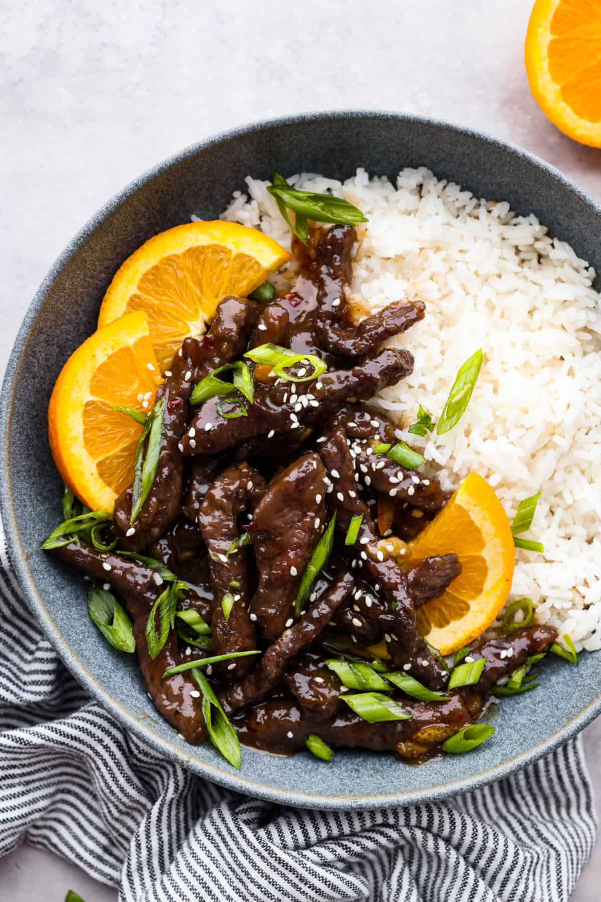 Orange beef served over rice, garnished with orange slices.