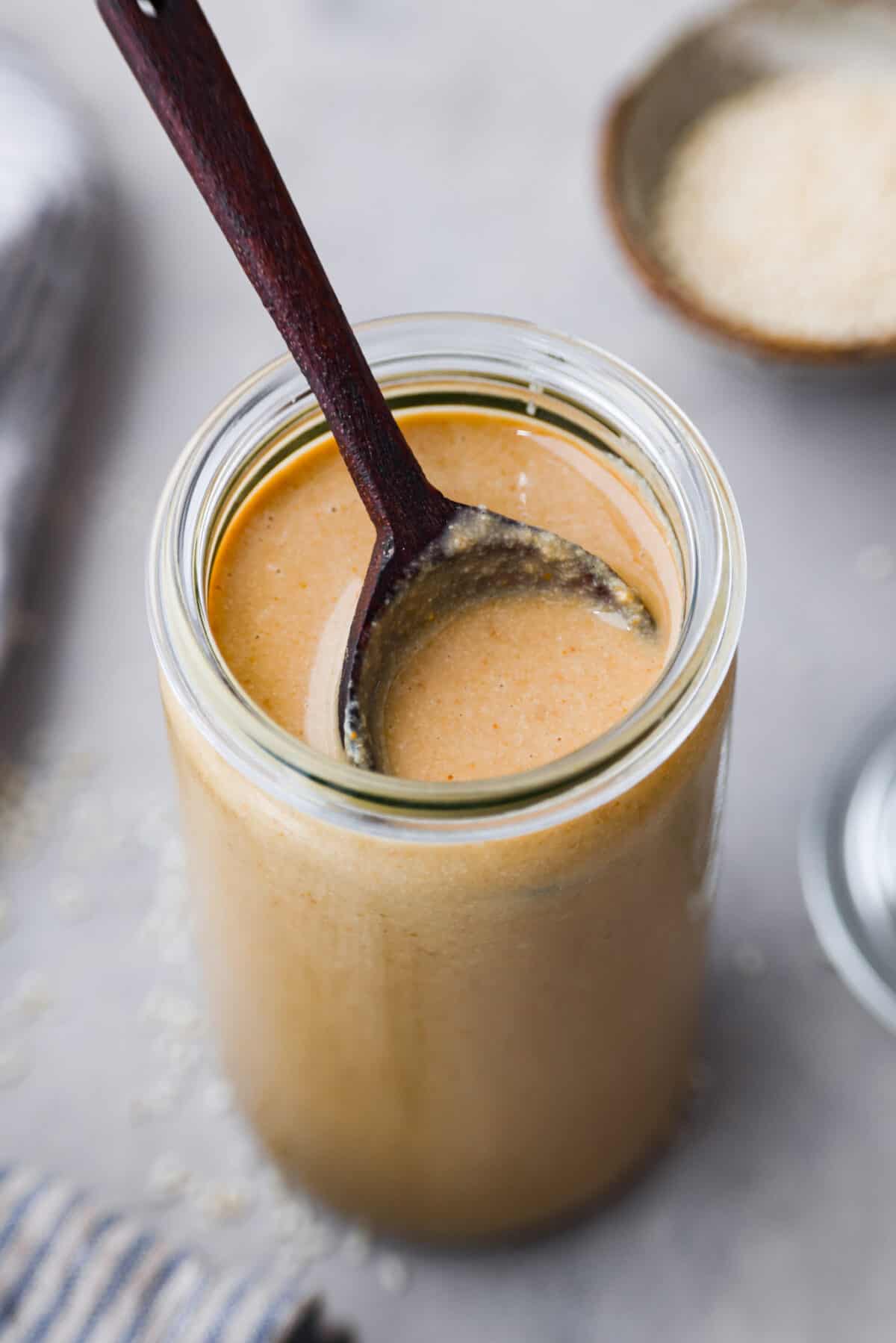 Close view of a wood spoon set inside a glass jar of tahini.