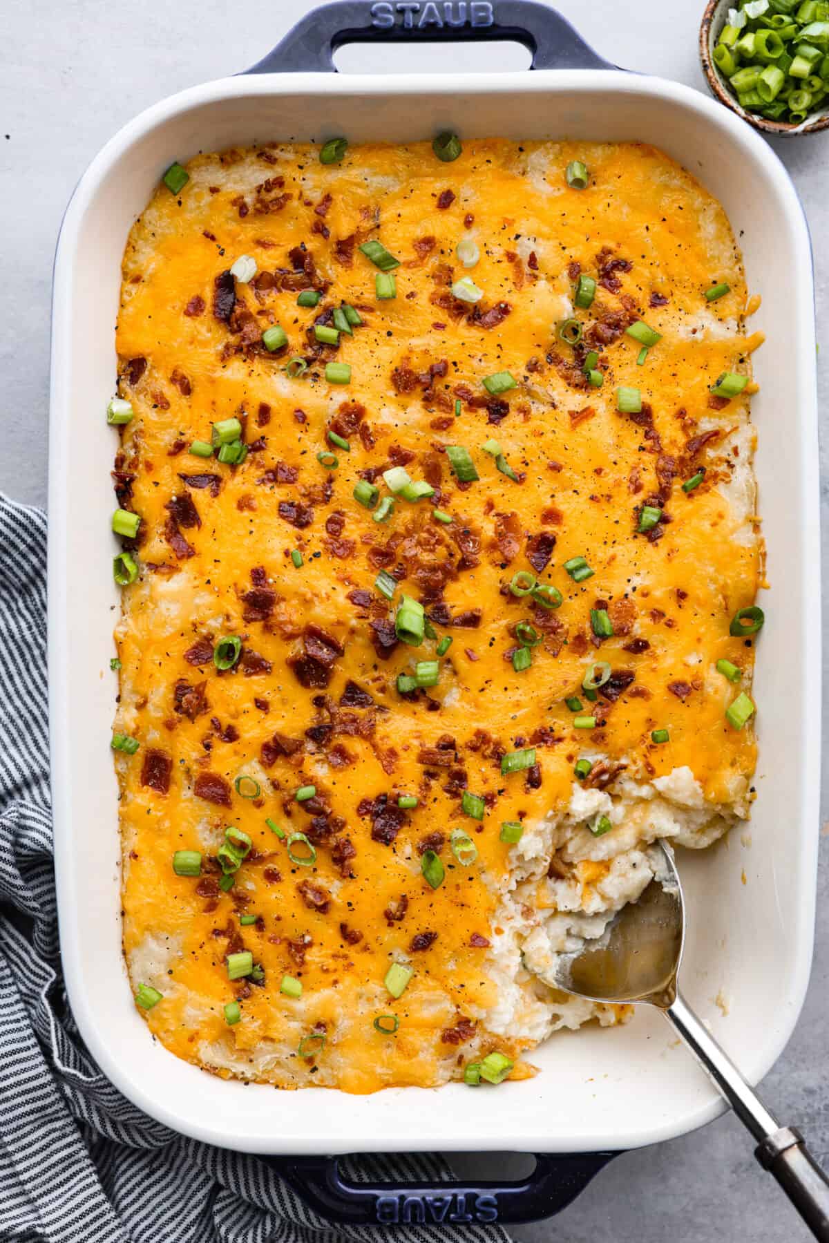 Top view of twice baked potato casserole in a blue casserole dish and garnished with green onions.