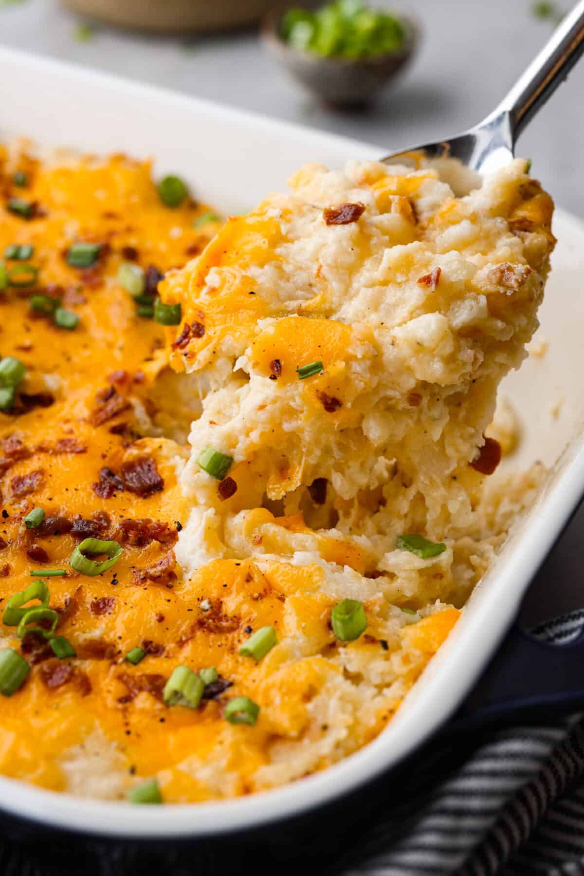 Close side view of twice baked potato casserole lifting out of a casserole dish.