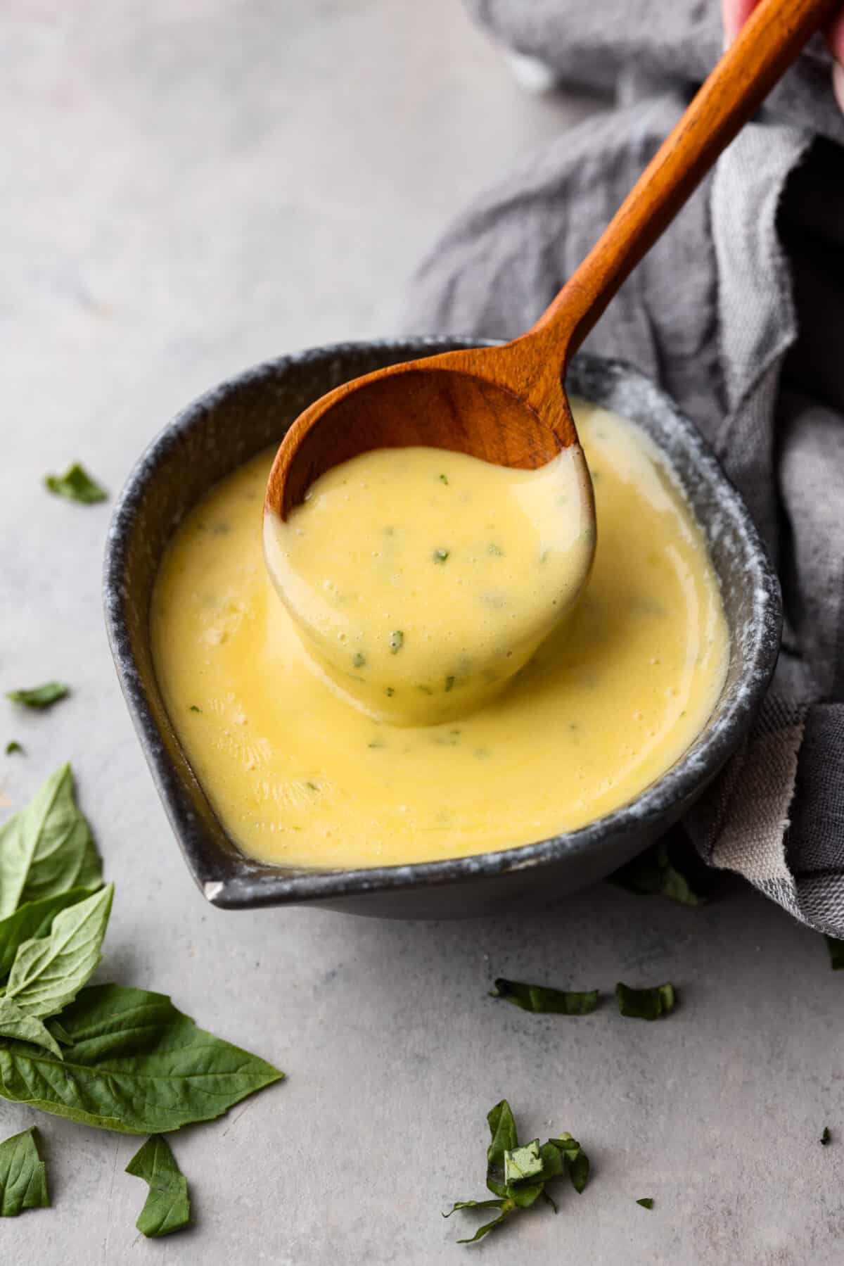 Bearnaise sauce in a bowl, being scooped up with a wooden spoon.