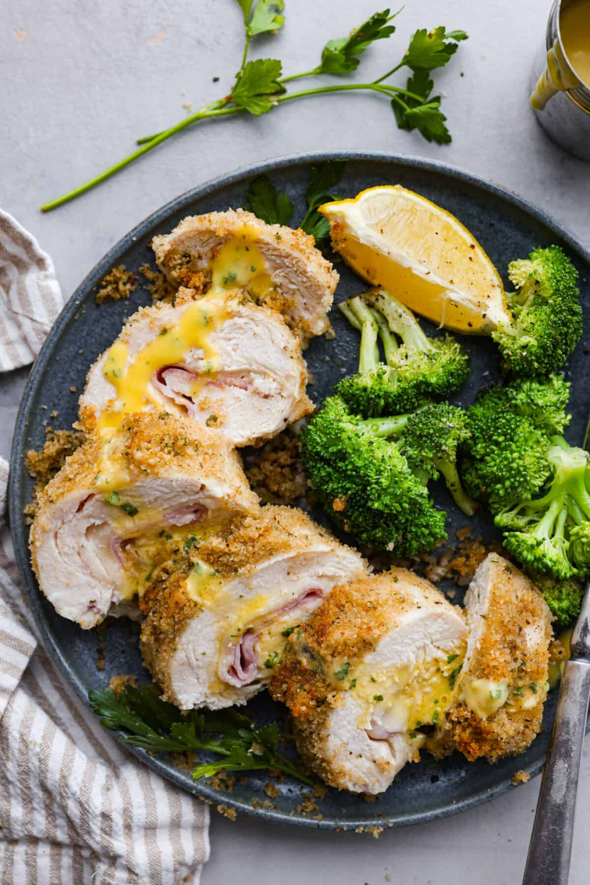 Overhead shot of plated chicken cordon bleu drizzled with sauce and  broccoli and a lemon wedge on the side. 