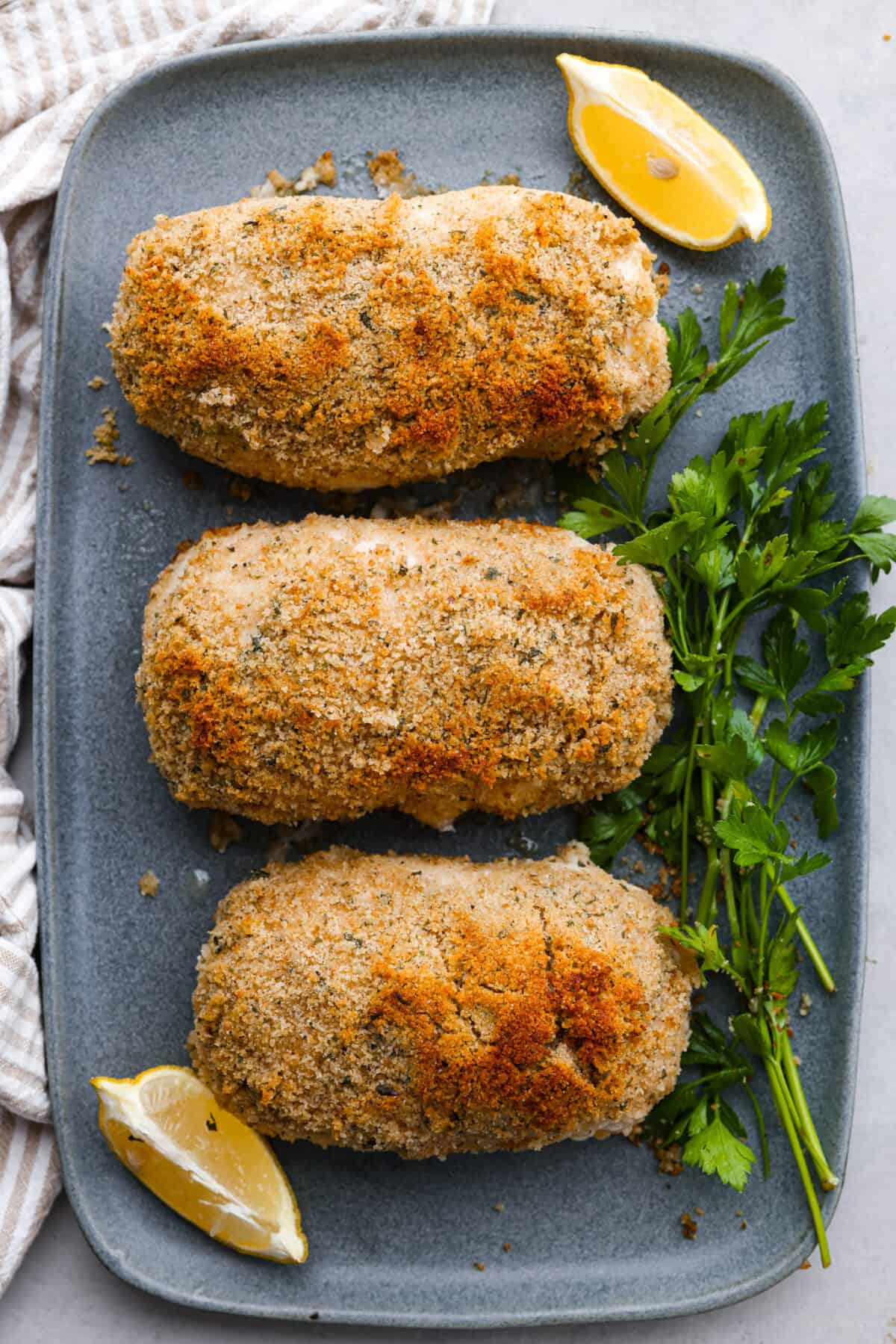 Top view of chicken cordon bleu on a gray platter garnished with lemon slices and fresh parsley leaves.