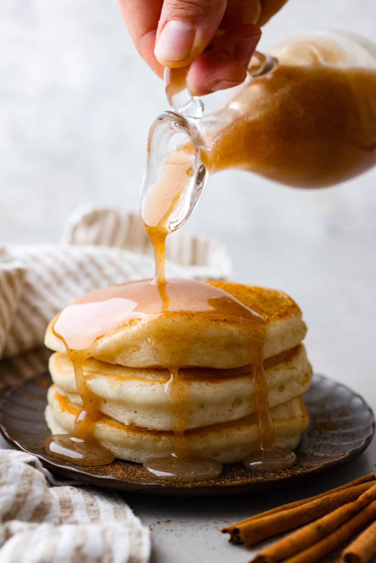 Side shot of someone pouring cinnamon syrup over a stack of pancakes. 