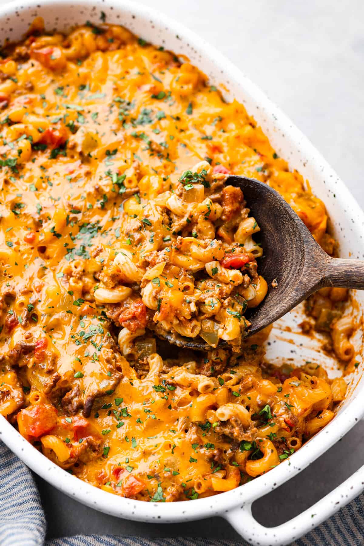 Taking a scoop of cheeseburger casserole with a wooden spoon.