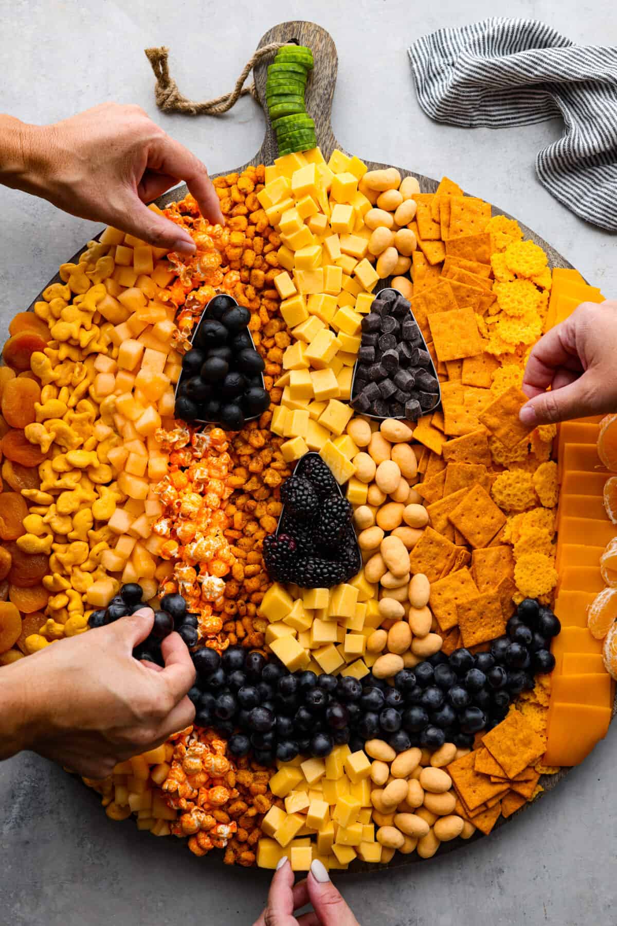 Overhead view of pumpkin charcuterie board with four hands reaching into grab snacks.