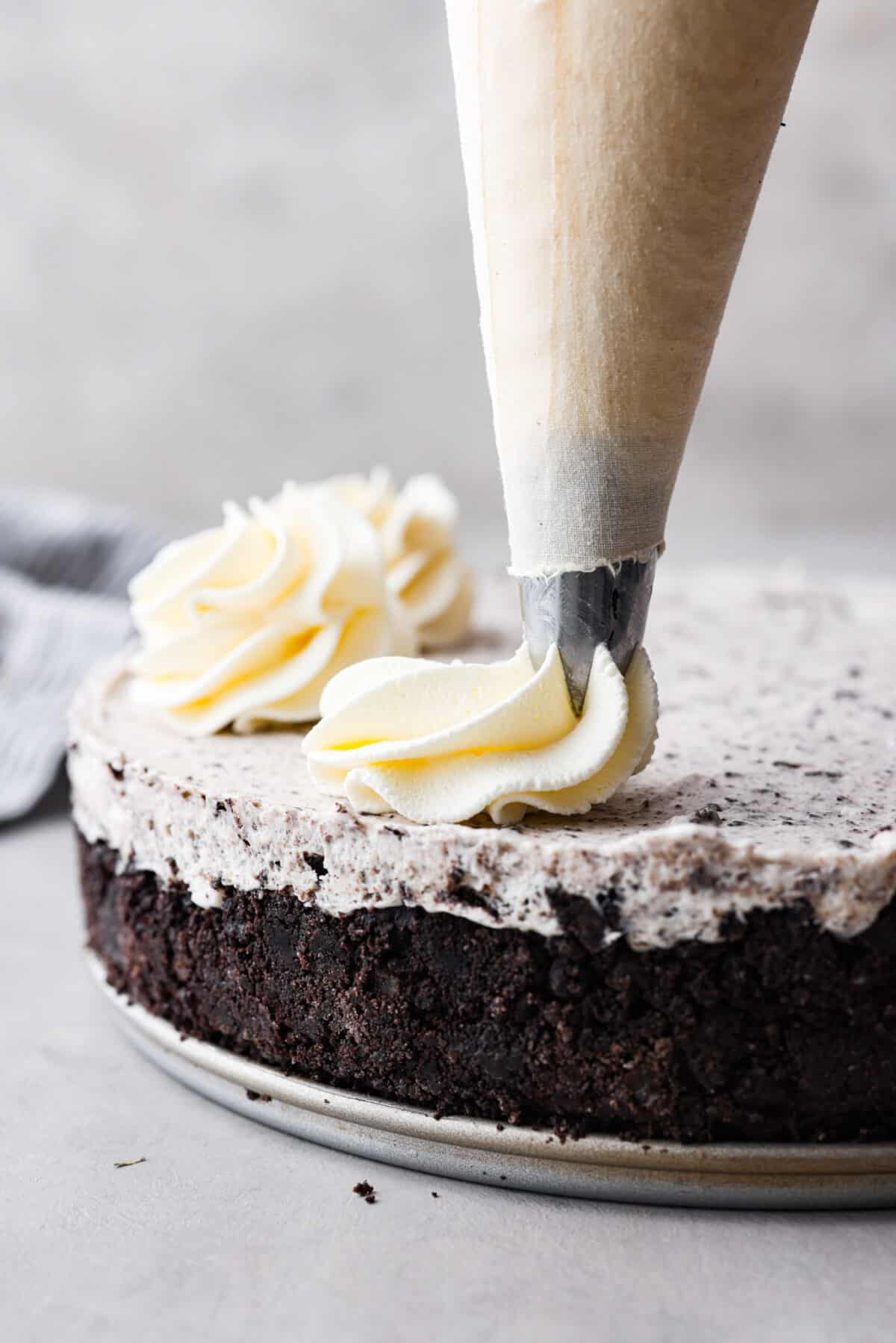 Close view of a piping bag piping stabilized whipped cream on an Oreo cheesecake.